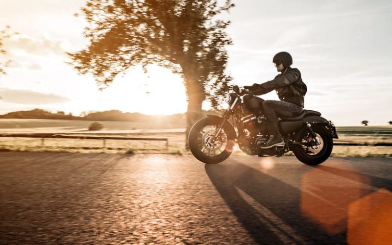 Man riding sportster motorcycle on countryside during sunset.