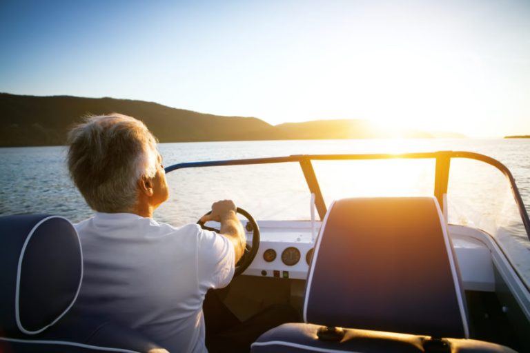 mature man driving speedboat on a lake at sunset