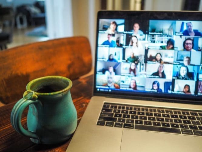 a cup of coffee beside a laptop with a virtual meeting on the screen